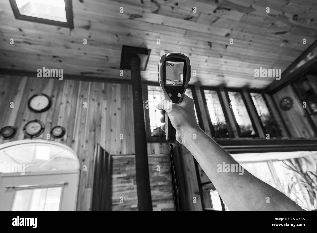 A close up and monochrome view of a home inspector using an IR thermal imaging camera to detect signs of cold bridging in a domestic property. Stock Photo