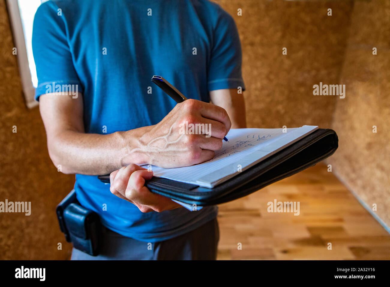 A close-up and front view of a professional male home inspector, using a blue pen to take notes on paper during an inspection of a domestic property. Stock Photo