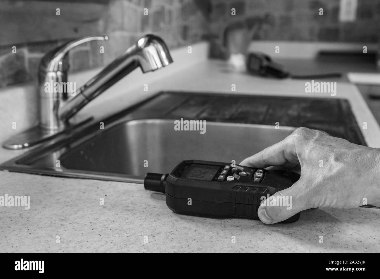 A close-up, black and white view of a person using an indoor air quality monitor, checking for pollutants and allergens inside a residential kitchen. Stock Photo
