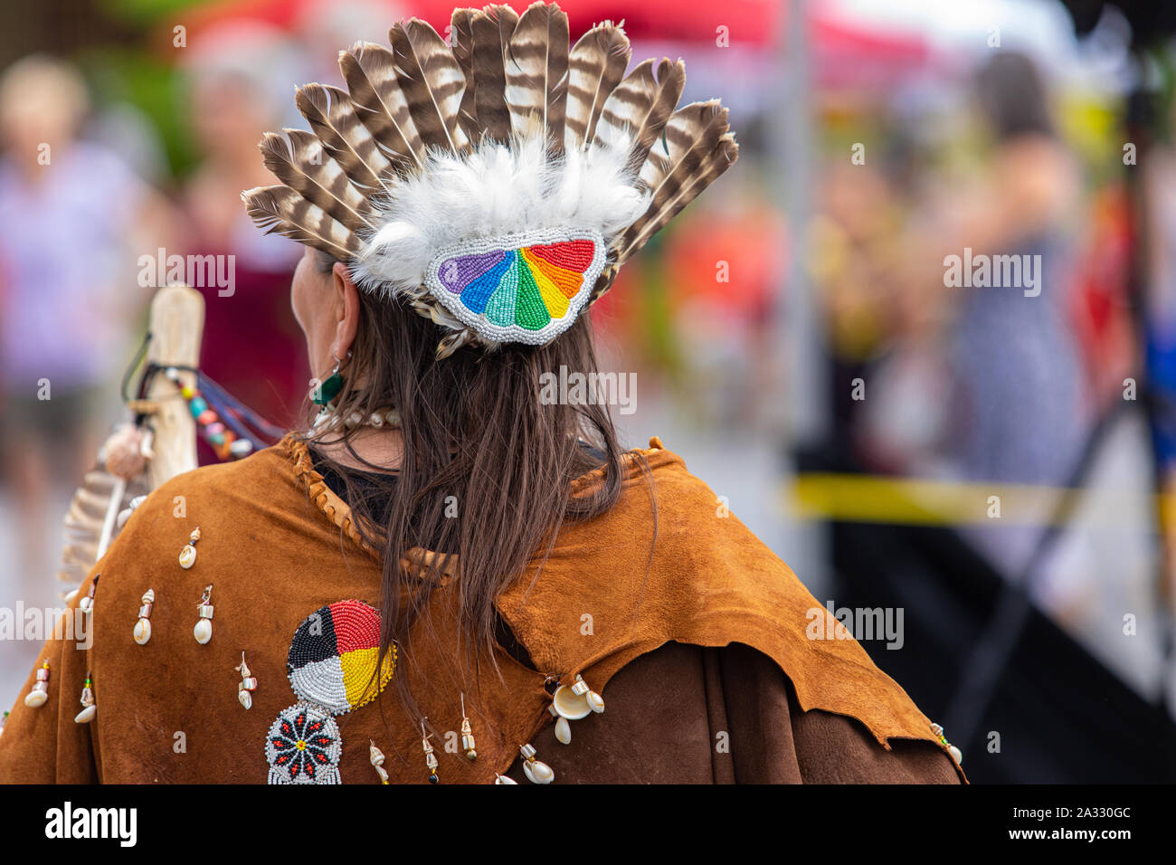 A close up view on the back of a woman's head, dressed in traditional indigenous costume, with eagle feathered headdress during a celebration of native culture. Stock Photo