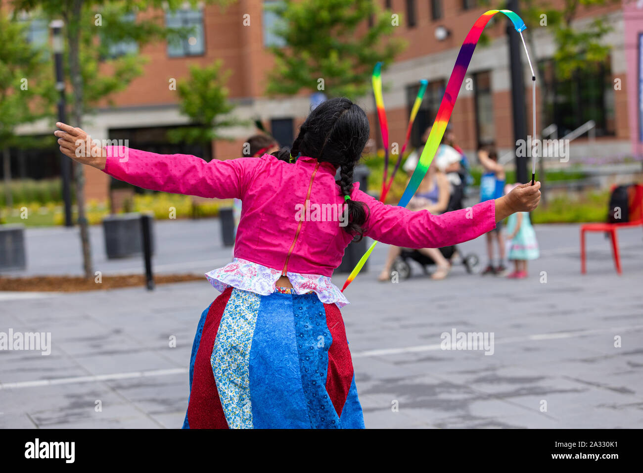 A close up and rear view of a female dancer dressed in vibrant clothes, ribbon twirling during a celebration of native music and culture. Stock Photo