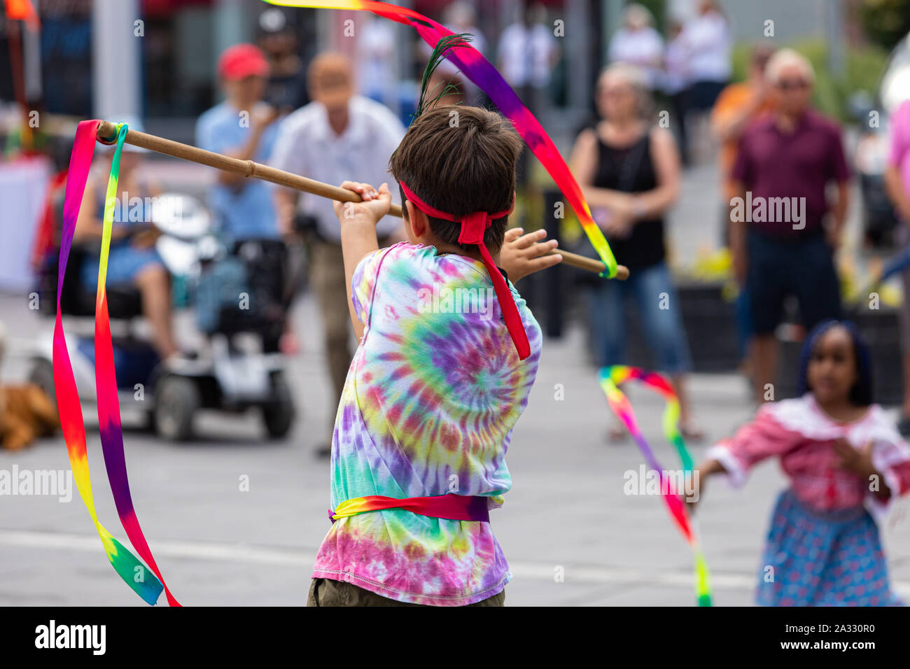 A close up view of a child performing a native dance ritual with vibrant colorful clothes, blurry people are seen in background with copy space. Stock Photo