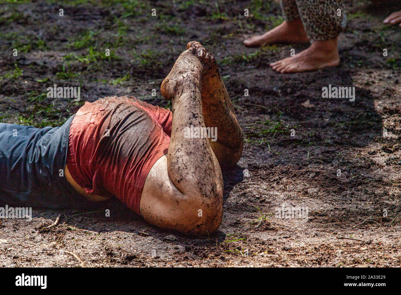 A young woman is seen closeup, laying on her stomach in mud and earth during a celebration of intercultural practices and rituals, with room for copy Stock Photo