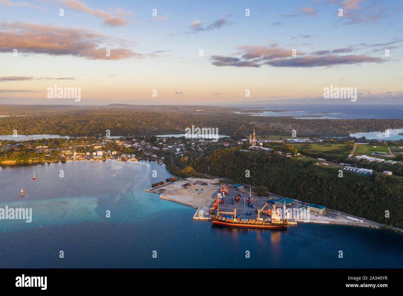 Aerial view of a container ship loading cargo in the commercial dock of Port Vila, Vanuatu capital city in the south Pacific at sunset Stock Photo