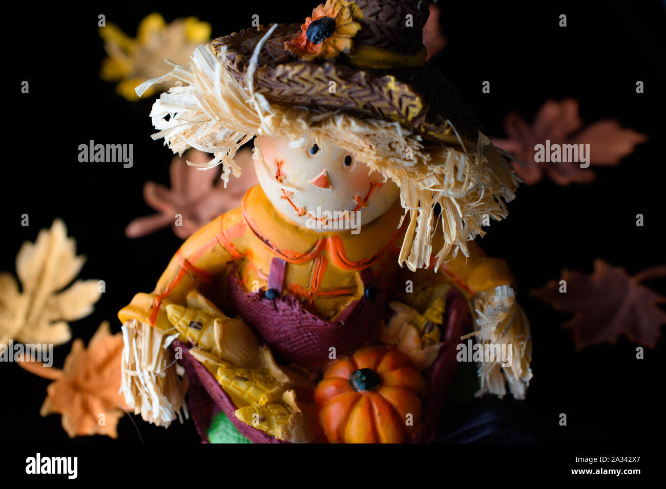 Adorable Happy Scarecrow Figurine Seated Among a Bed of Autumn Leaves Stock Photo