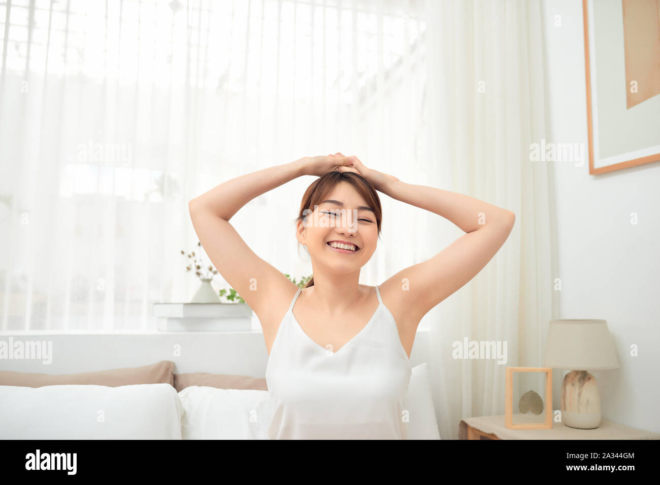 Happy Asian girl waking up stretching arms sitting on the bed in the ...