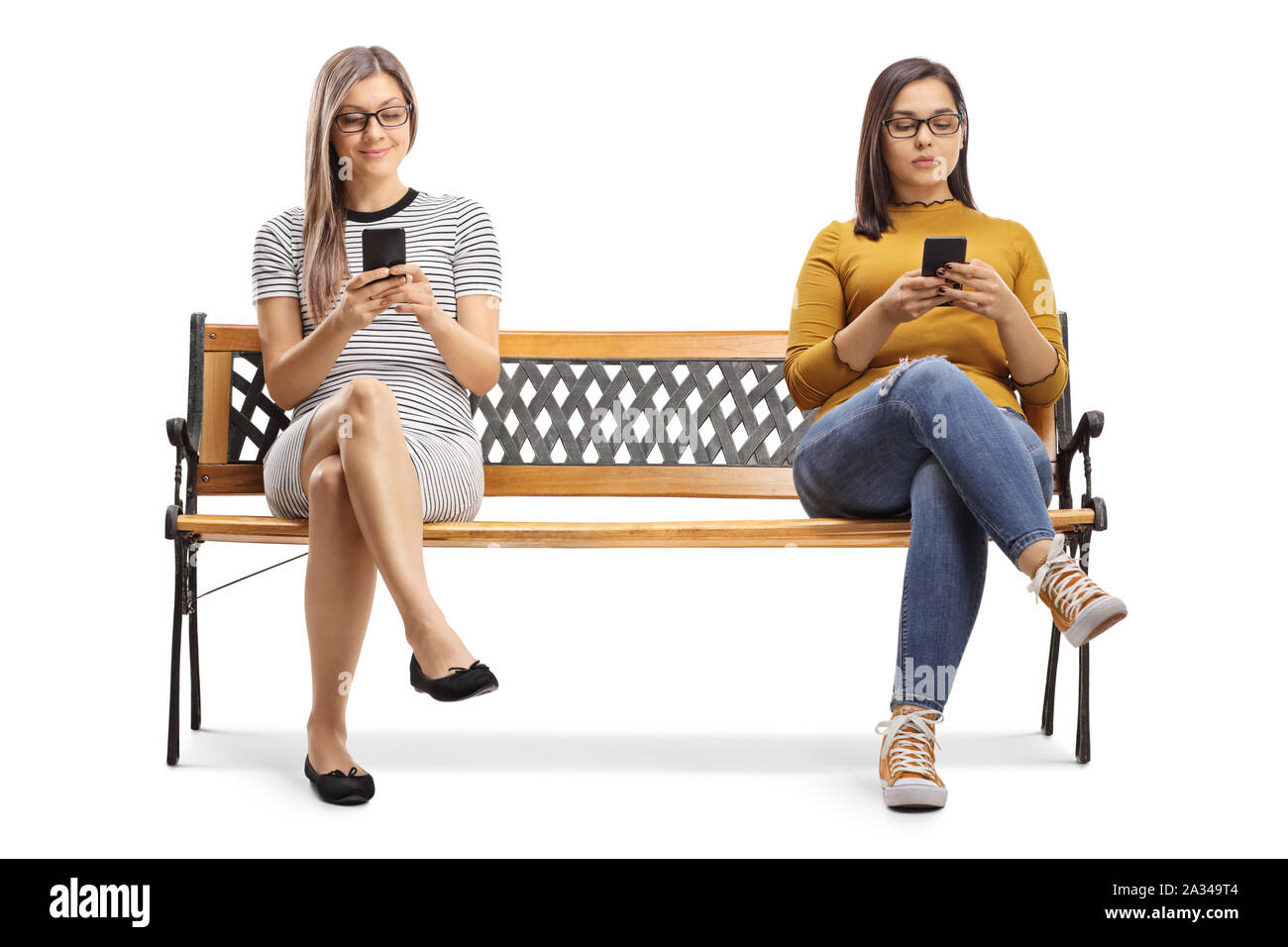 Two young women sitting on a bench and typing on smartphones isolated on white background Stock Photo