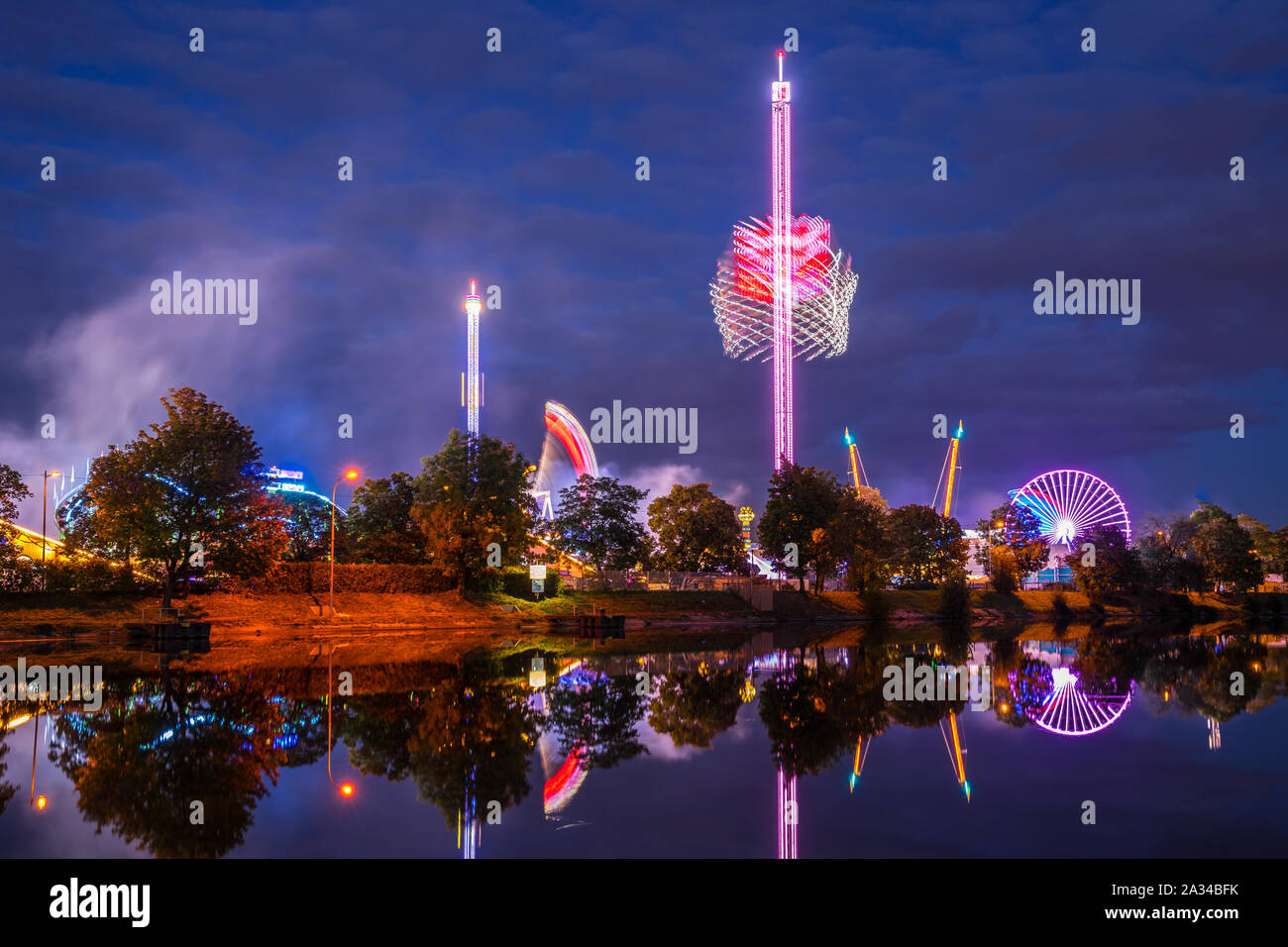 Germany, Colorful illuminated big wheel and rollercoaster of giant swabian fair called cannstatter wasen in stuttgart bad canstatt reflecting in water Stock Photo