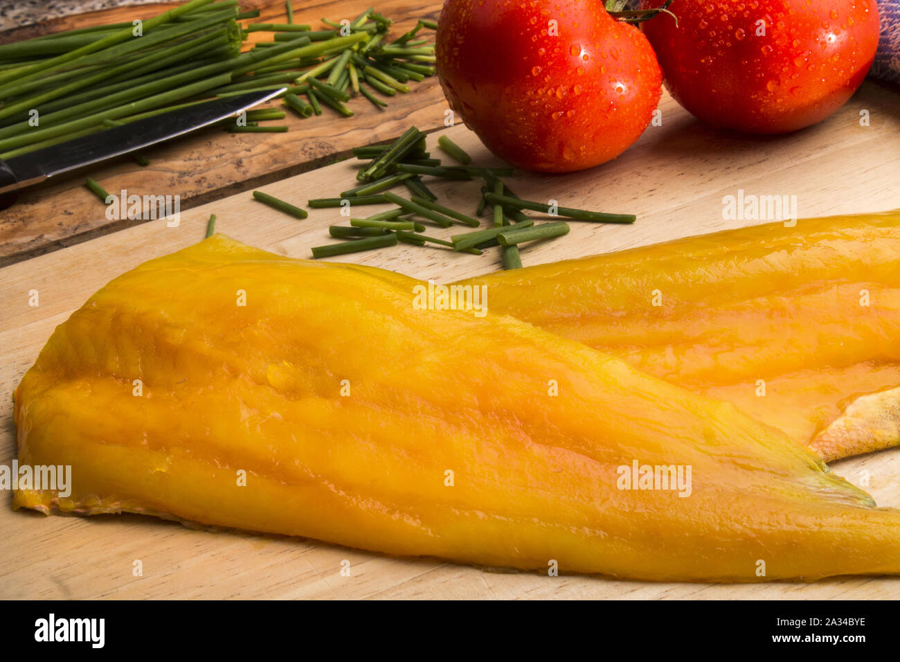 smoked haddock fillet on a wooden board, fresh tomato and chive in the background Stock Photo