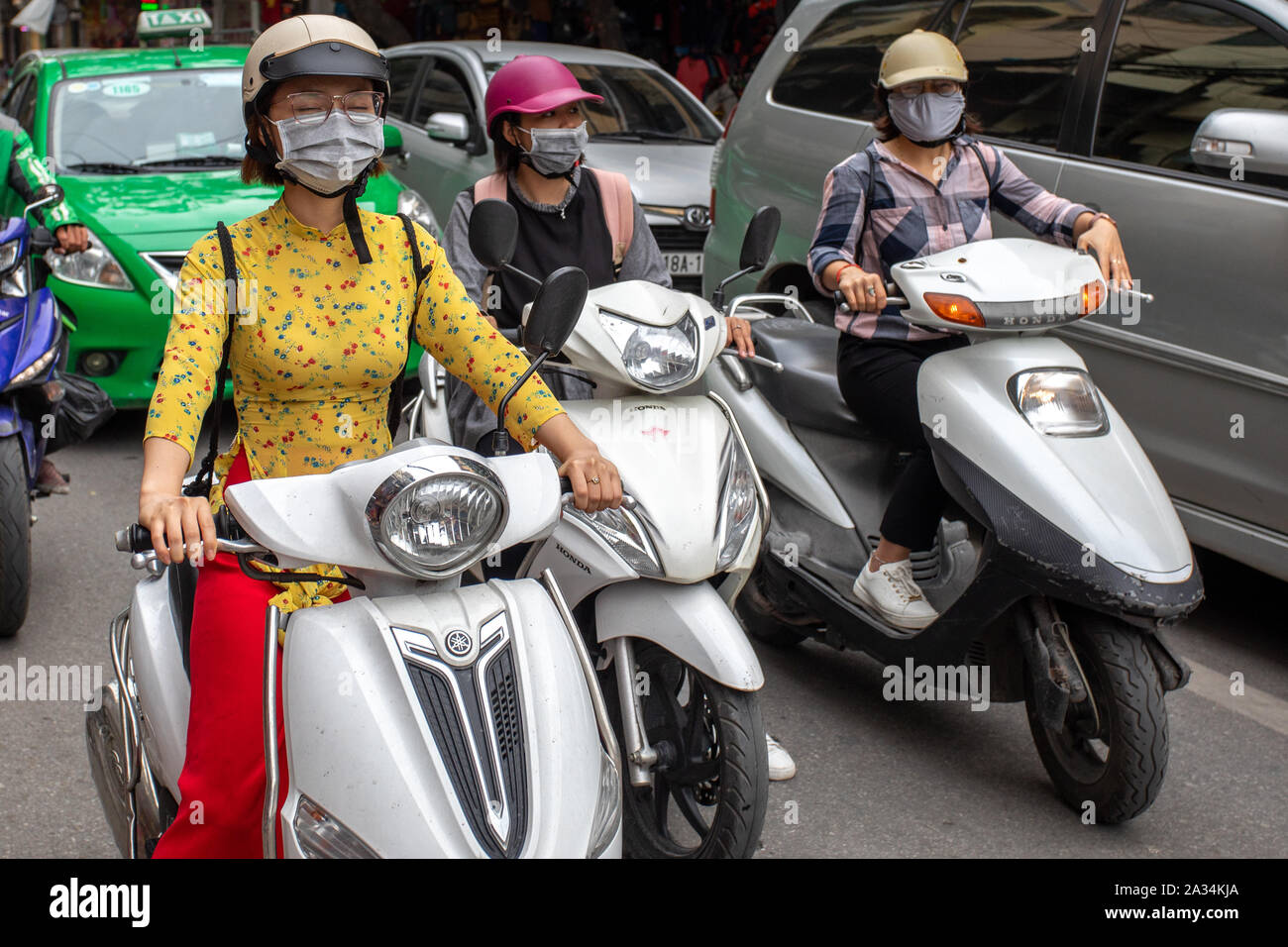 Three young females with pollution mask on motorcycles at the street of Hanoi, Vietnam. Pollution are huge problem in southeast asia. Stock Photo