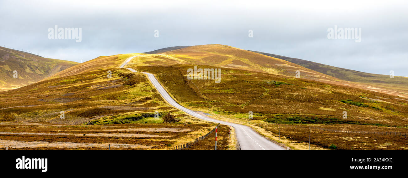 A scenic highway through bright yellow and brown highlands during autumn season in Cairngorms national park, Scotland Stock Photo