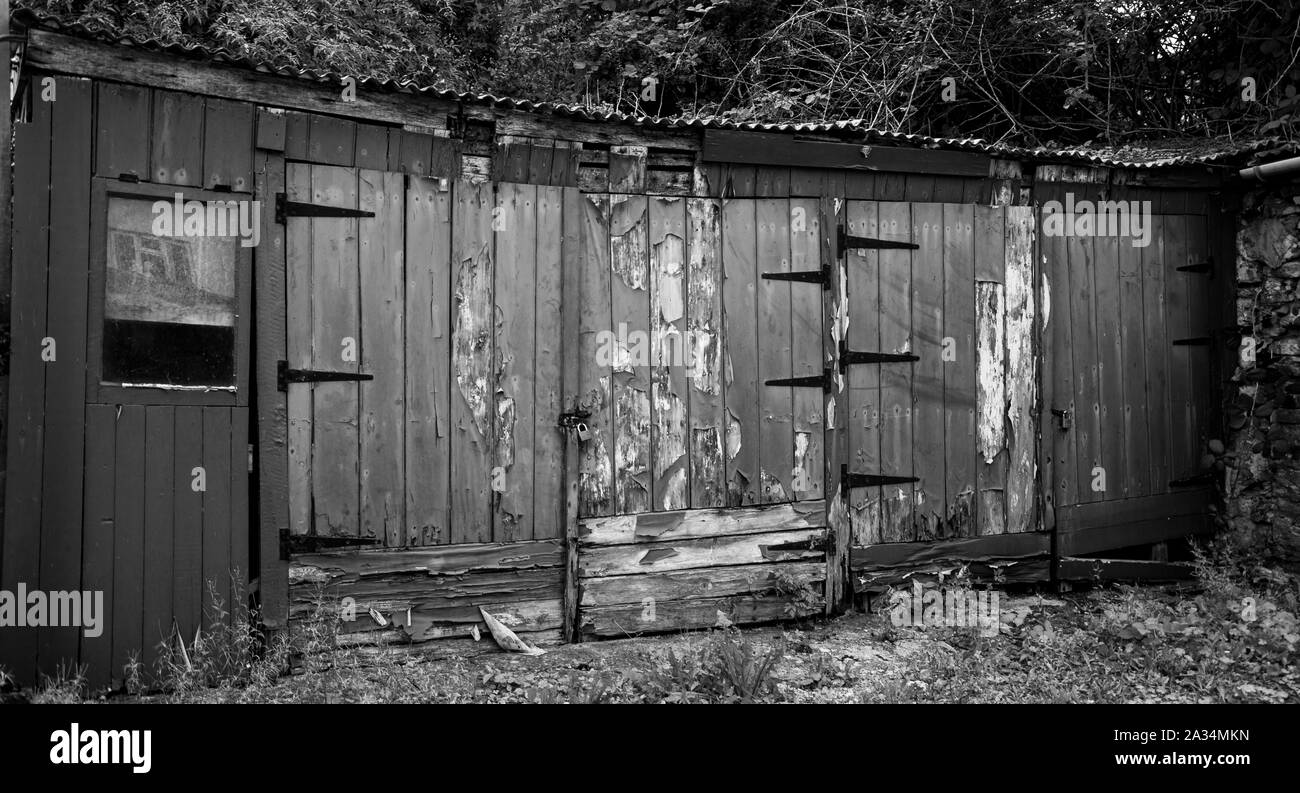 Black and white image of a row of dilapidated shed doors with peeling paint Stock Photo