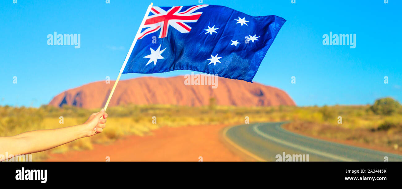 Woman's hand waving an Australian flag Red Centre Outback. Tourism in Northern Territory, Central Australia. Banner panorama of Uluru Ayers Rock in Stock Photo