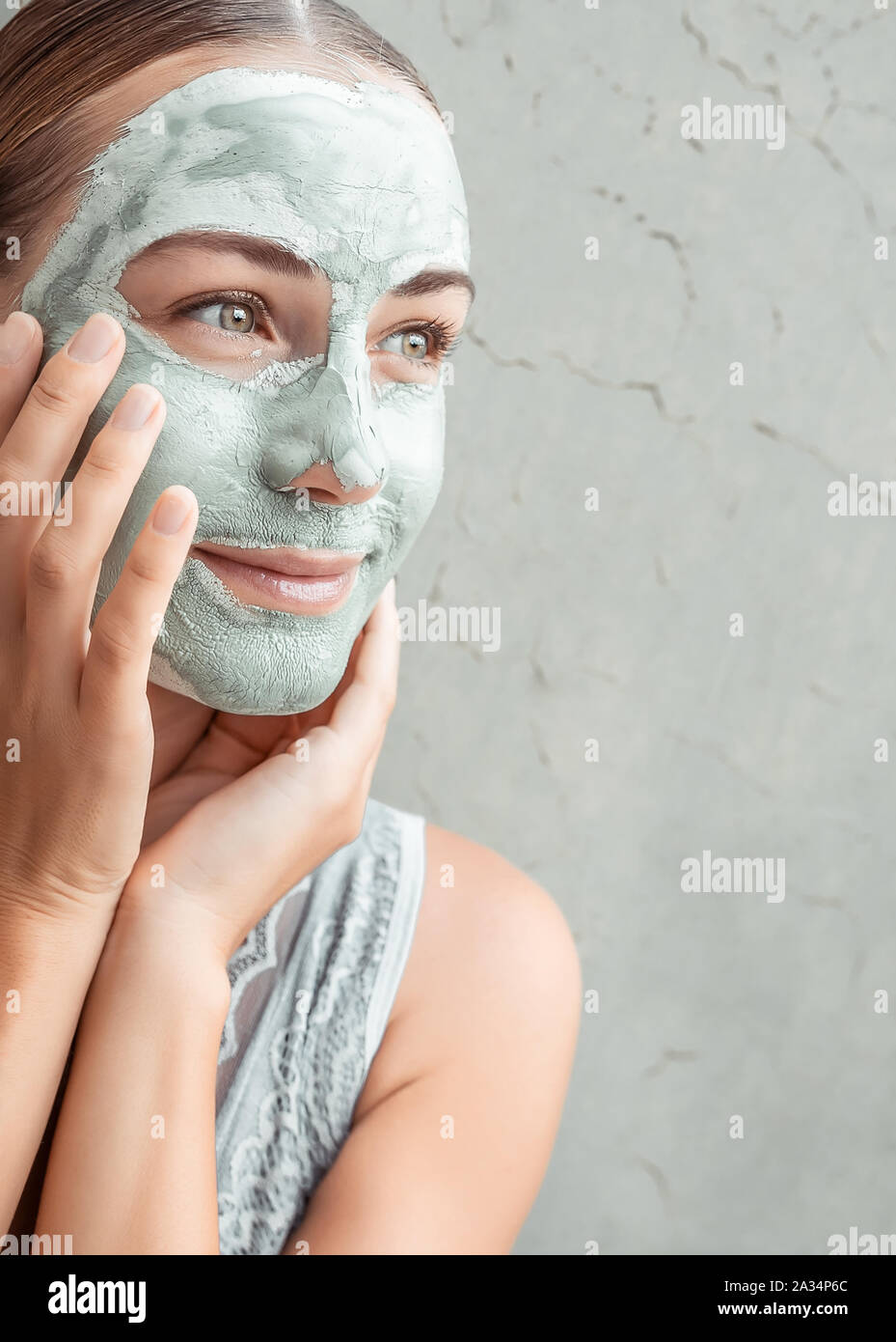 Portrait of a happy woman doing facial mask of a blue clay, with pleasure touching face with her hands, pampering and beauty treatment concept Stock Photo