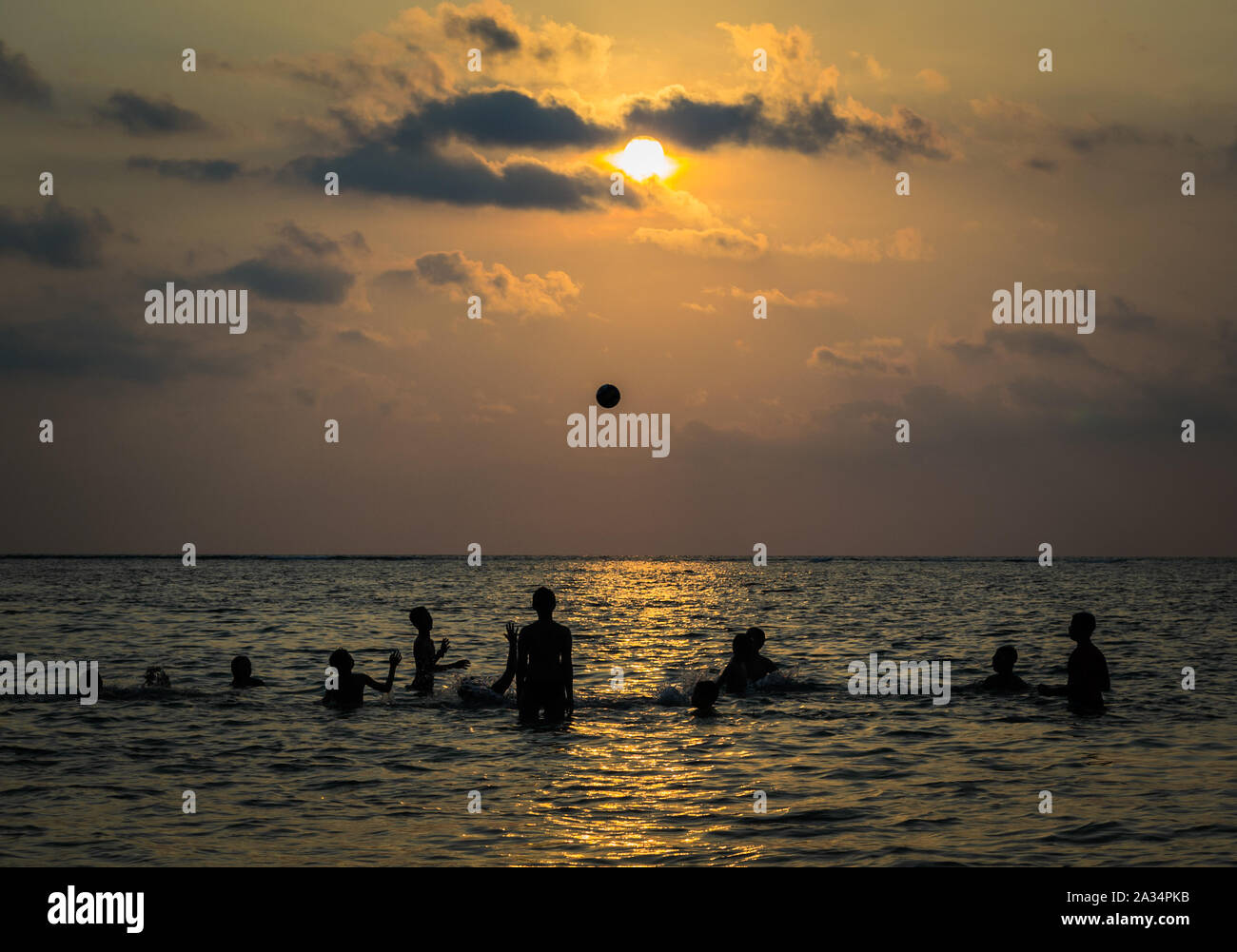 silhouetted group of boy are playing a ball in the sea during sunset Stock Photo