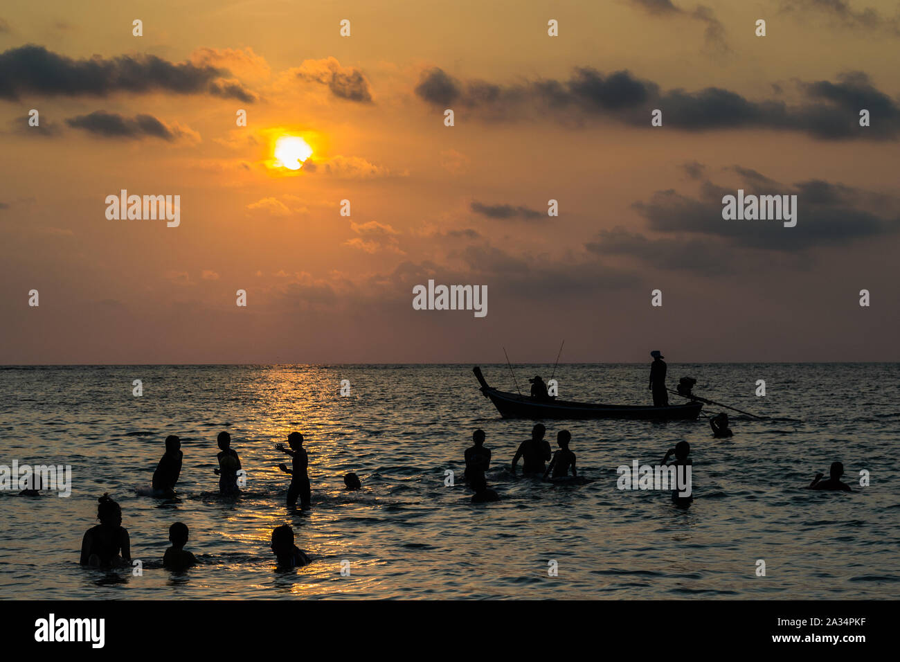 silhouetted group of people are playing in the sea with a long tail boat during sunset Stock Photo