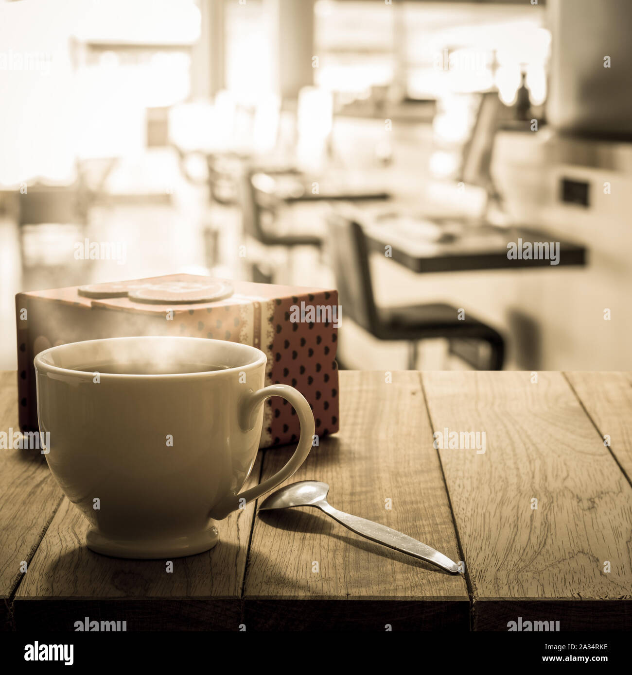 Hot coffee and gift box on wooden table in the internet cafe in warm tone Stock Photo