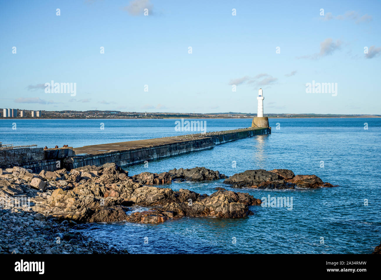 Rocky shore at South breakwater lighthouse near entrance to Aberdeen port and harbor, Scotland Stock Photo