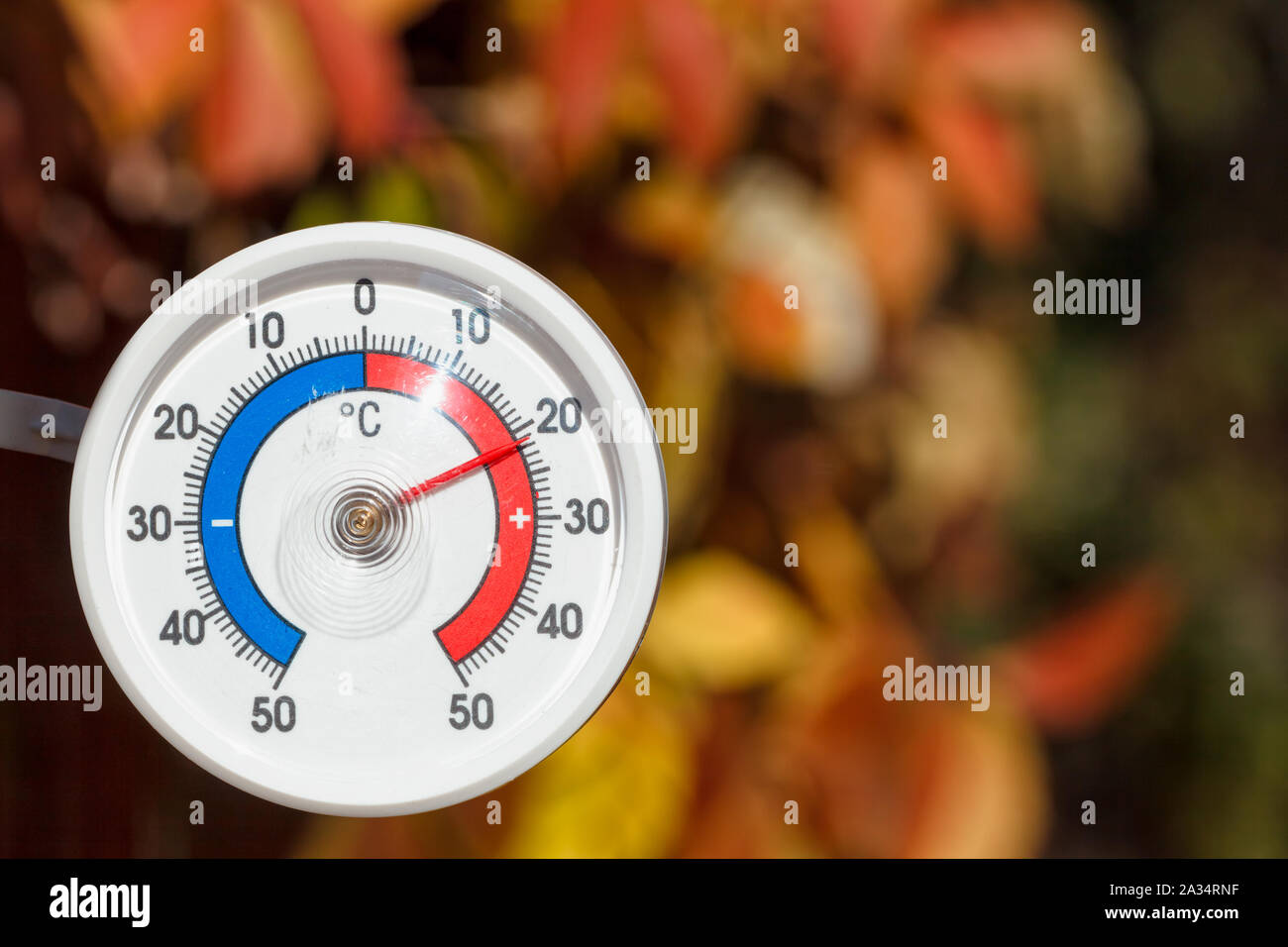 Outdoor thermometer with celsius scale showing warm temperature, blurred autumn leaves seen in background - hot indian summer or global warming concep Stock Photo