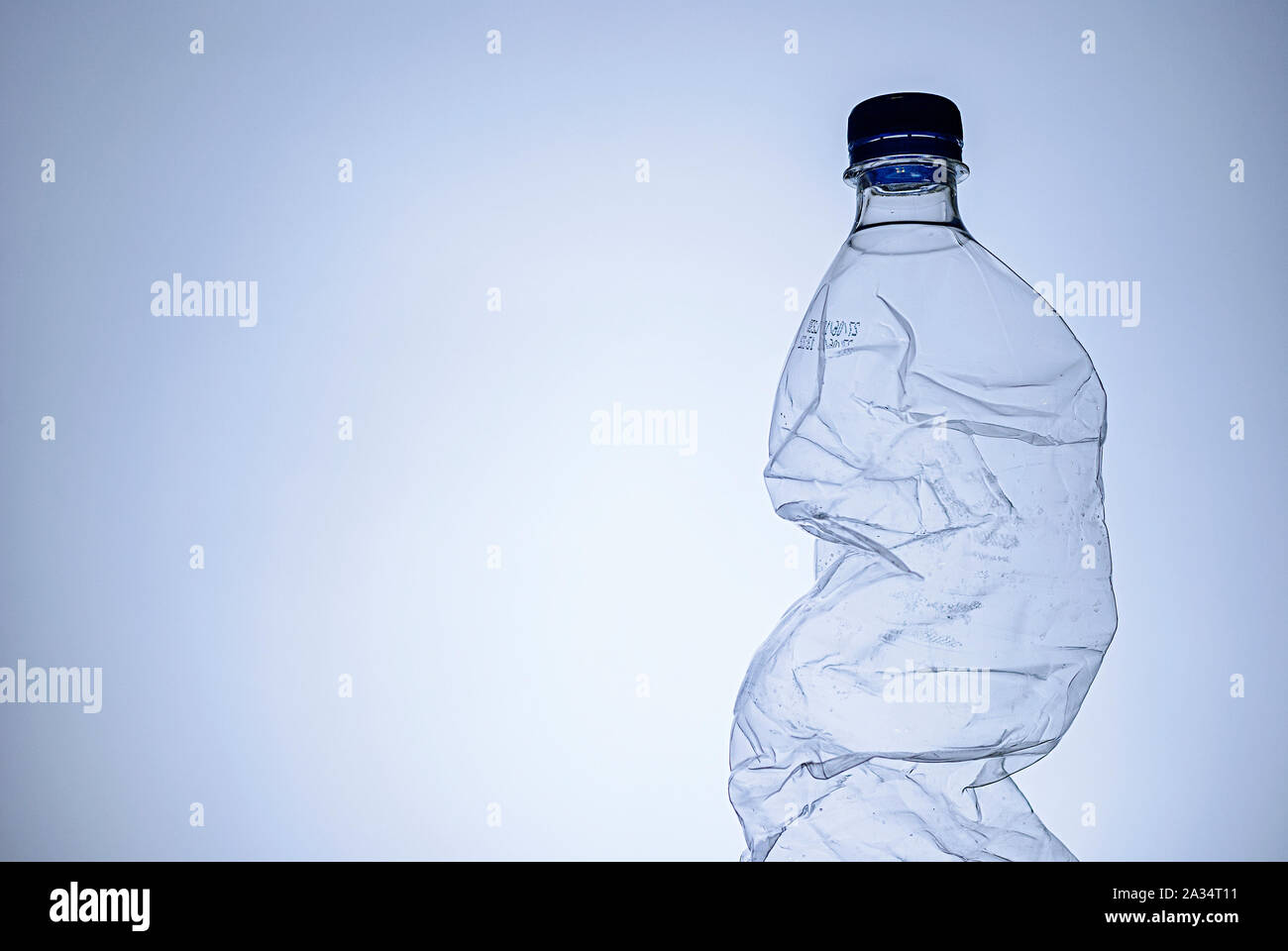 Crumpled clear empty plastic bottle with lid as a side border over blue with copy space conceptual of disposable plastics and pollution Stock Photo