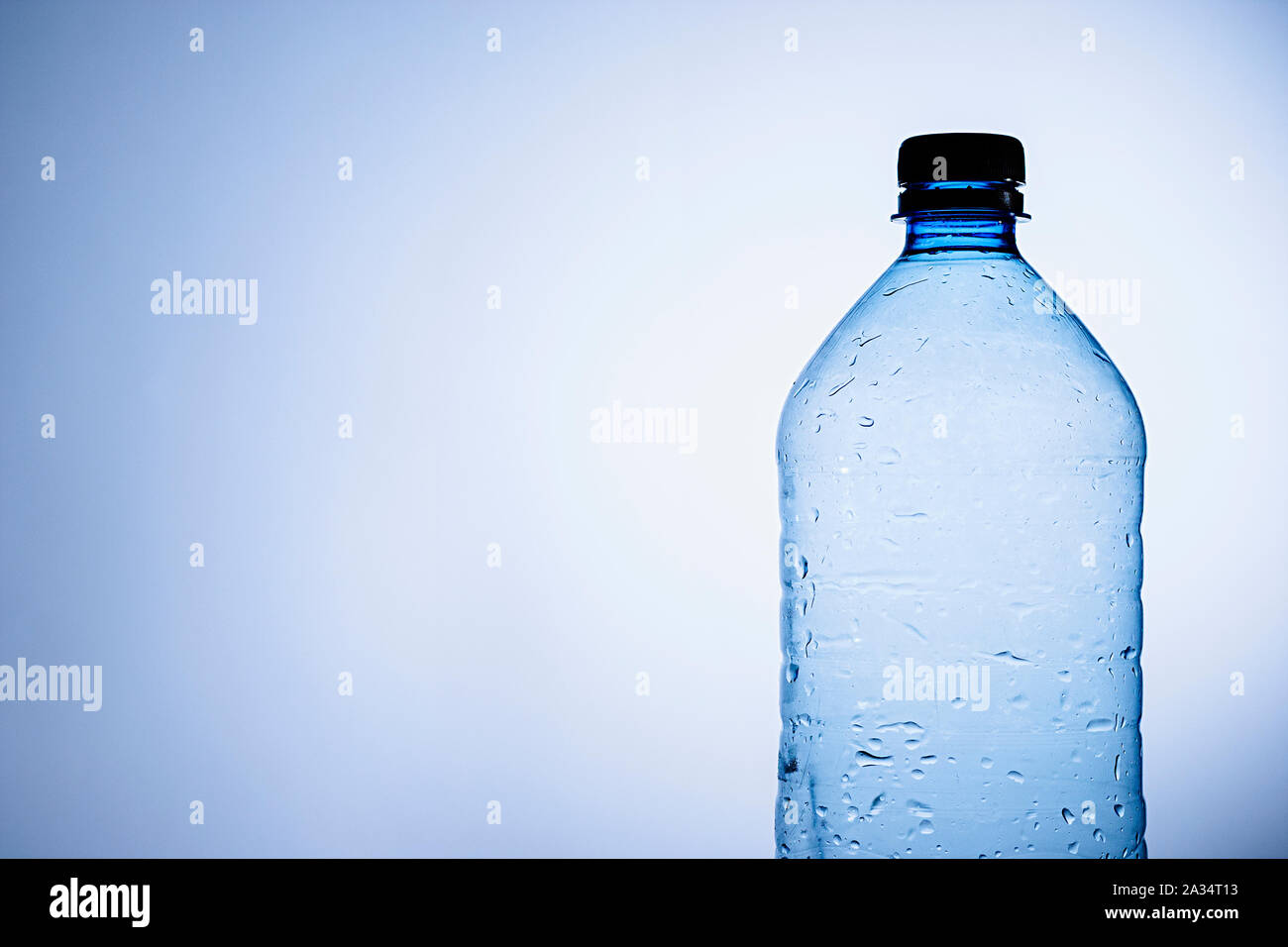 Clear plastic bottle of chilled water or liquid with condensation droplets on the surface of the bottle over blue with copy space Stock Photo
