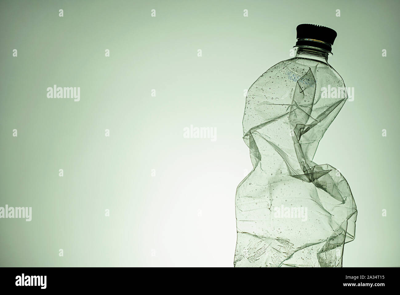 Crumpled clear empty plastic bottle with lid as a side border over green with copy space conceptual of disposable plastics and pollution Stock Photo