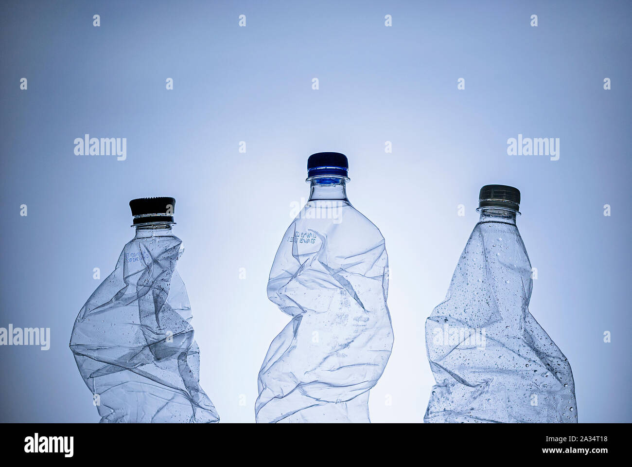 Three empty clear wet plastic bottles for recycling over a blue background in a conceptual image Stock Photo