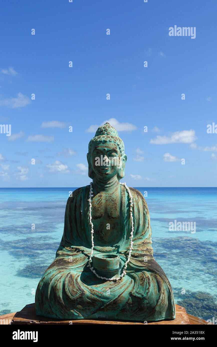 A figure of Buddha in front of a turquoise lagoon on the island of Fakarava in French Polynesia in the South Pacific; copy space Stock Photo