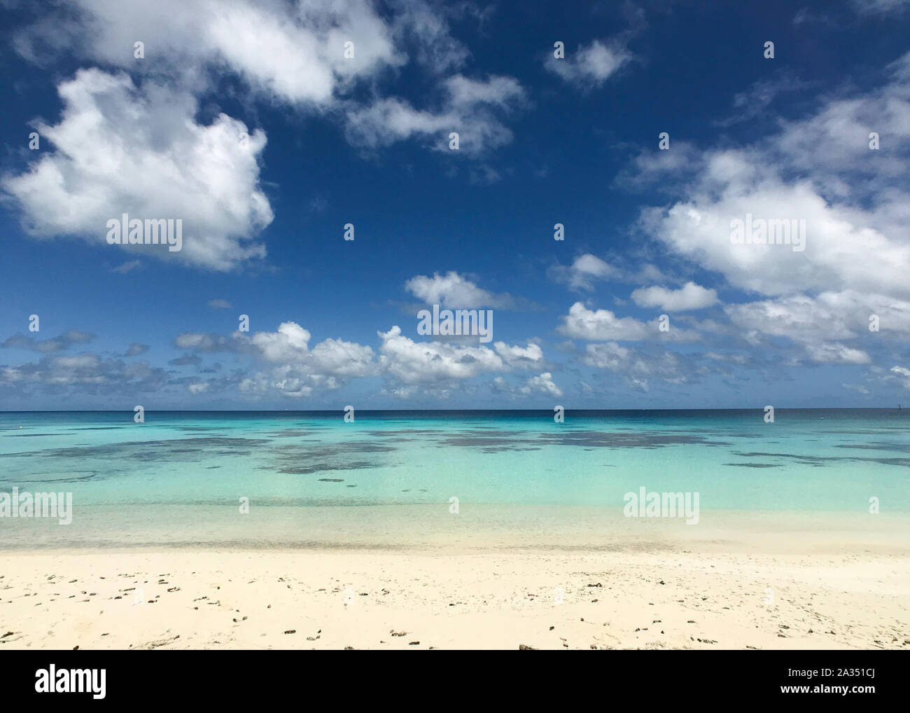 A white sandy beach leads into a turquoise lagoon under a bright blue sky with clouds and copy space; background Stock Photo