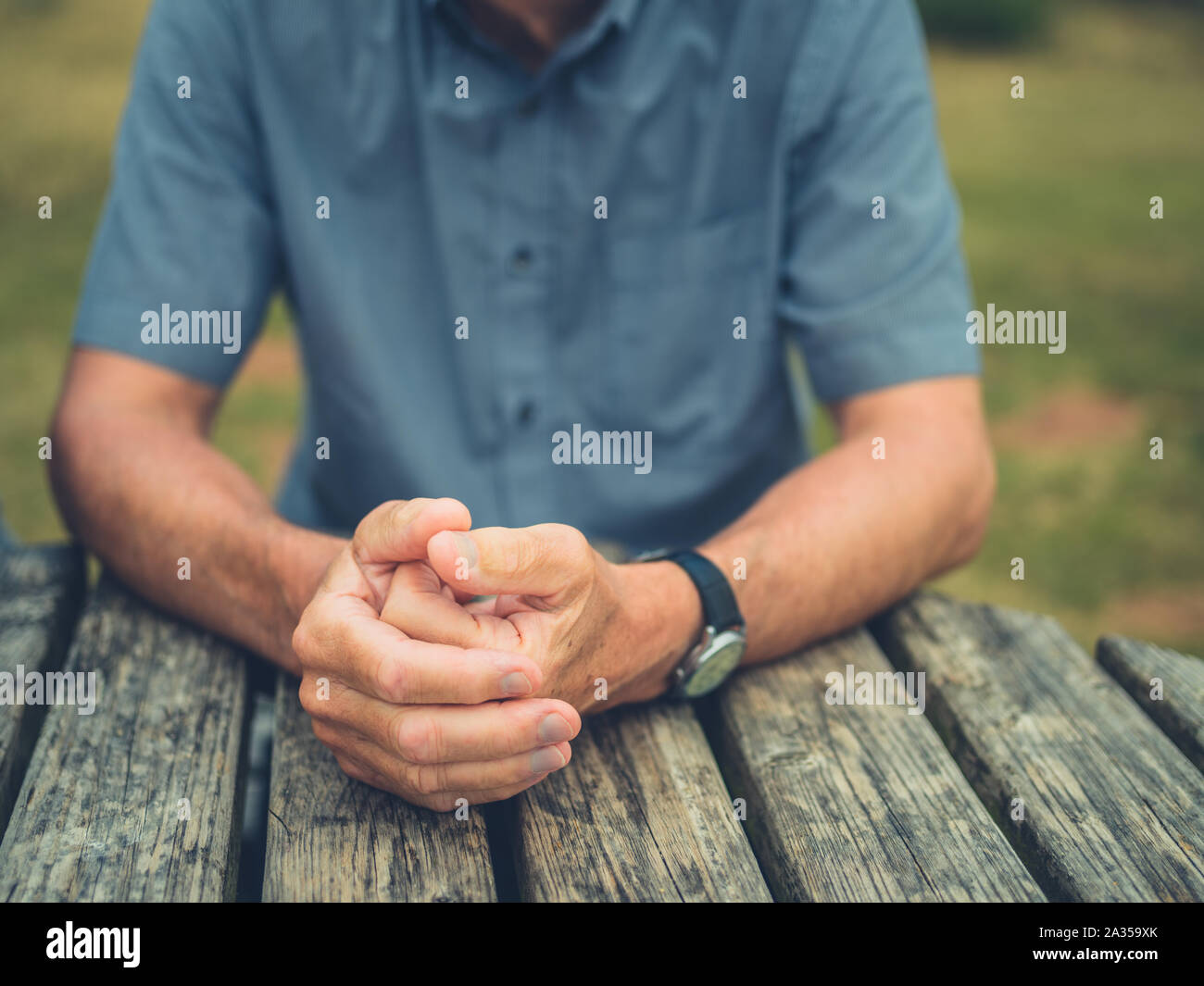 A senior man is resting his hands on a table outdoors Stock Photo