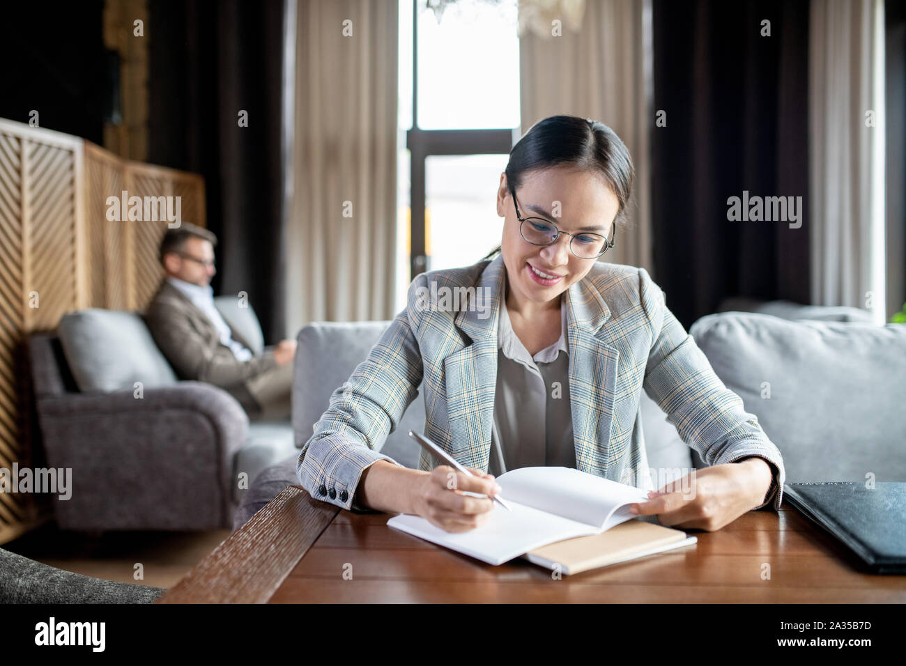 Happy young female student making notes in copybook while preparing for lesson Stock Photo
