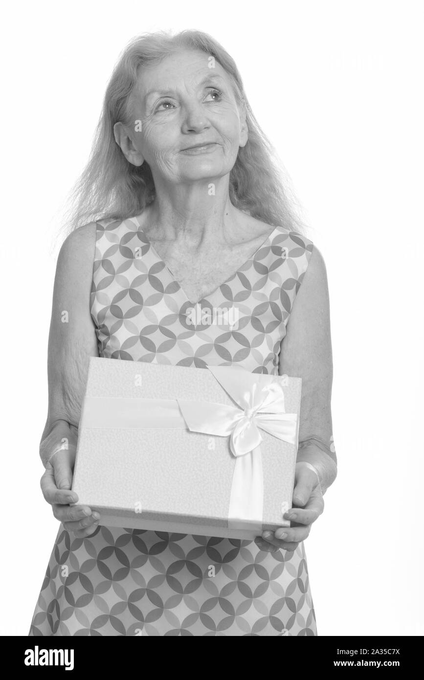 Studio shot of senior woman holding gift box while thinking Stock Photo