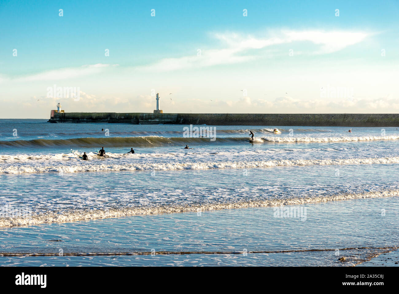 People surf waves near South breakwater lighthouse, Aberdeen beach, Scotland Stock Photo