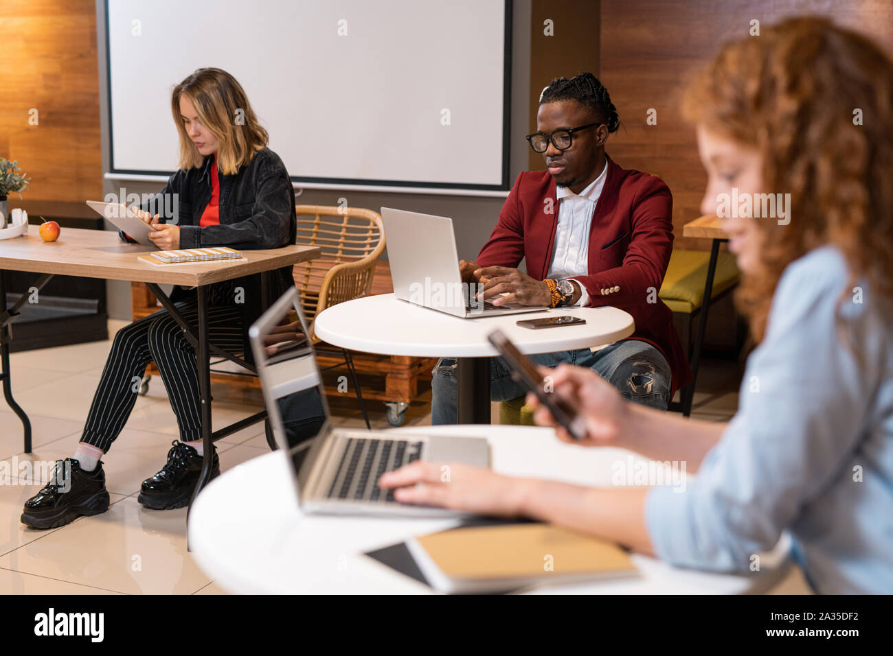 Group of multicultural students using mobile gadgets while preparing homework Stock Photo