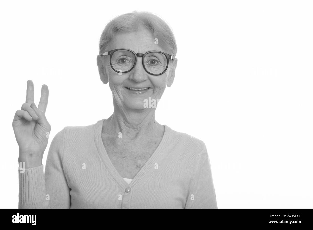 Happy senior nerd woman smiling while giving peace sign and wearing geeky eyeglasses Stock Photo
