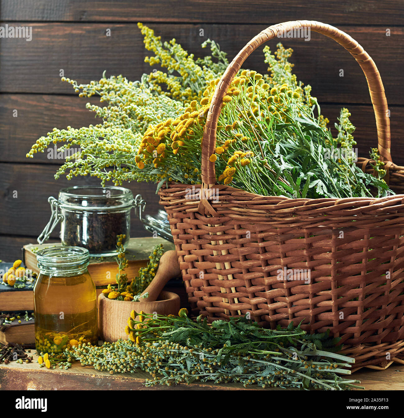 Herbal helminthic triad: absinth, tansy and cloves; fresh herbs in the wicker basket and wooden mortar, on old books,  healing infusion is nearby, clo Stock Photo