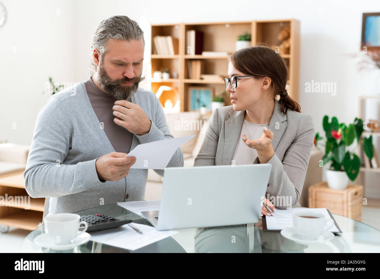 Pensive bearded man looking through paper while listening to real estate agent Stock Photo