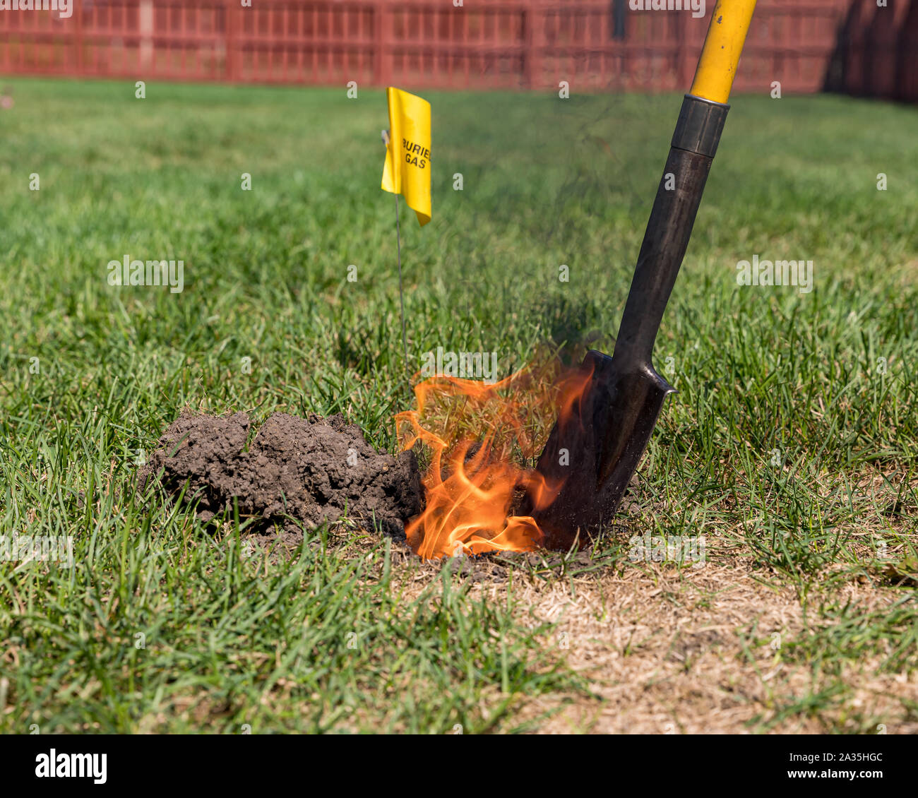 Real black smoke and flames rise from fire in hole of yard. Yellow natural gas warning sign, plastic pipe, shovel. Concept of notify utility company Stock Photo