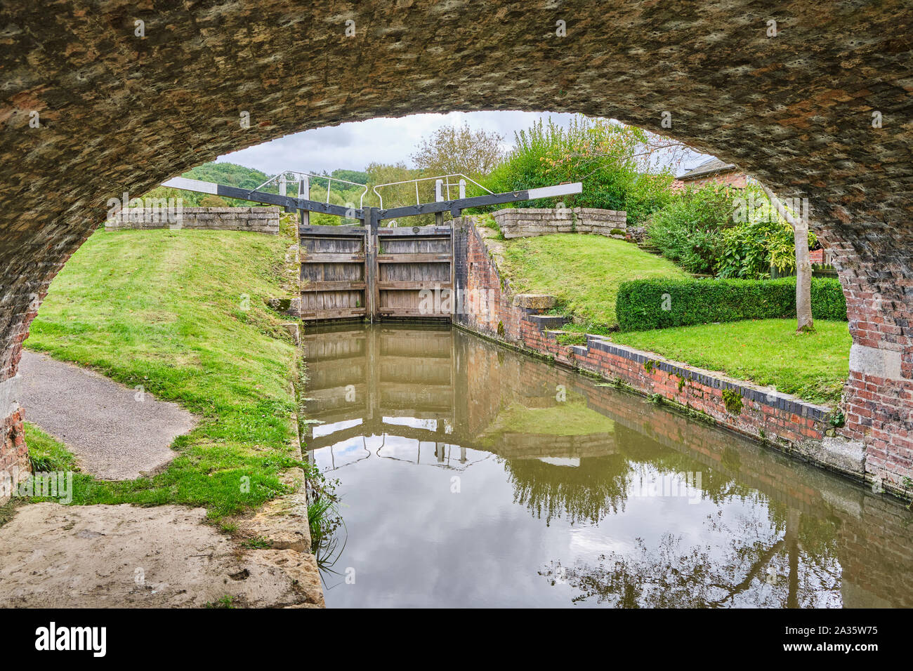 Lock gates on the Grantham Canal at Woolsthorpe by Belvoir framed by the arch of a towpath bridge Stock Photo