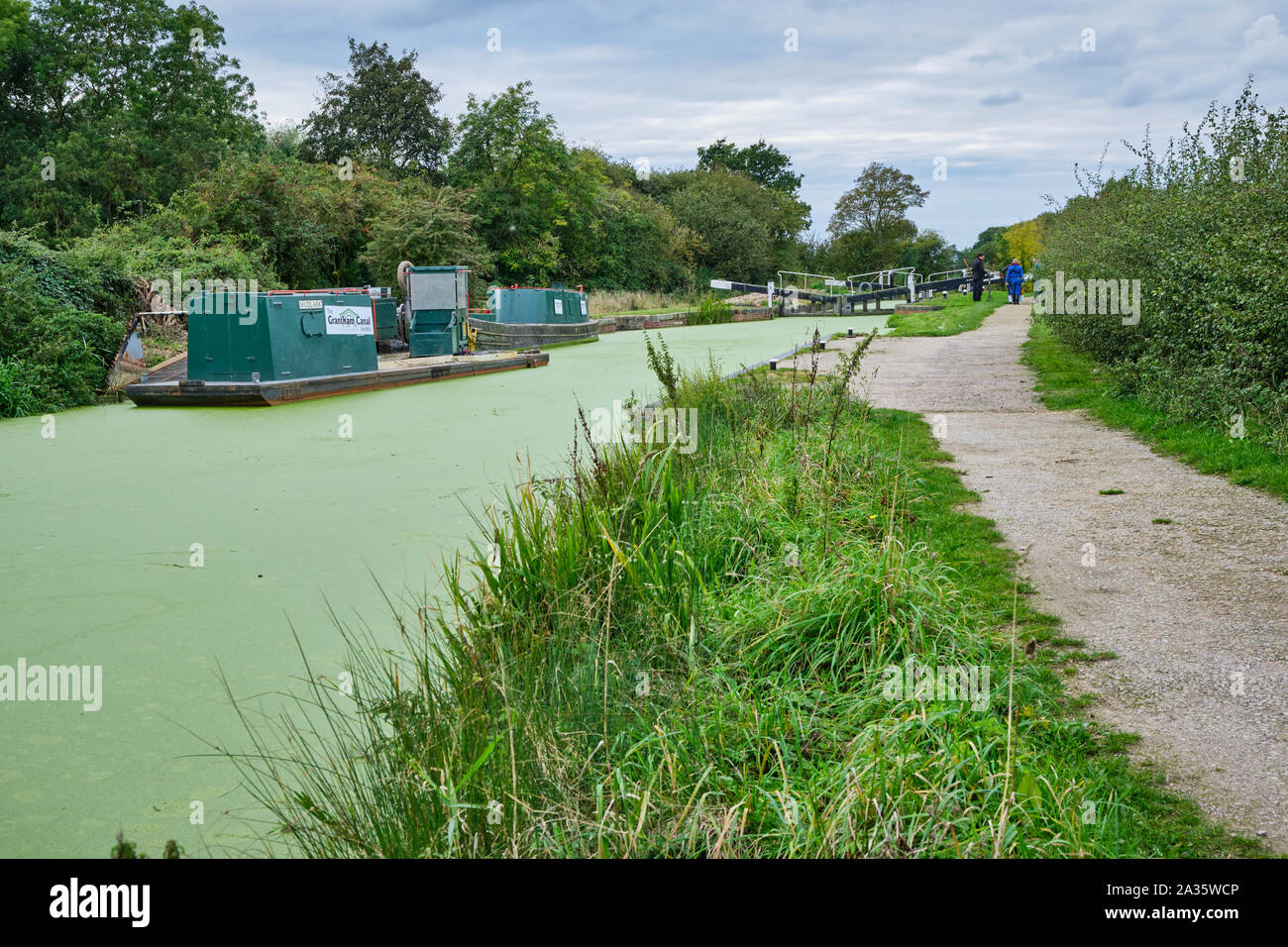 Boats moored at the side of an algae covered Grantham canal by the towpath near the lock gates at Woolsthorpe By Belvoir Stock Photo