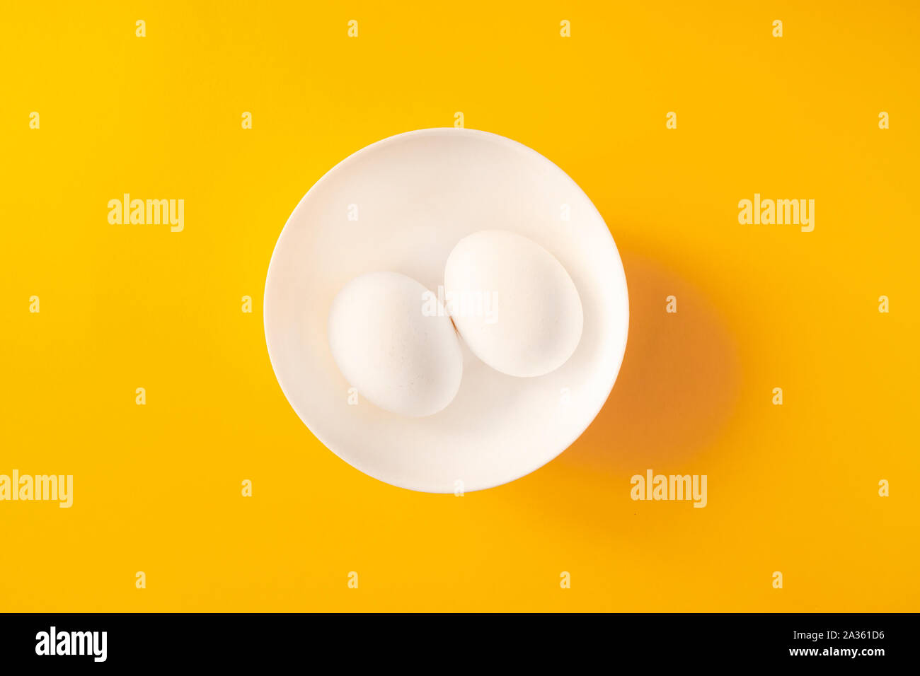 Two white eggs in a bowl on yellow background. Stock Photo