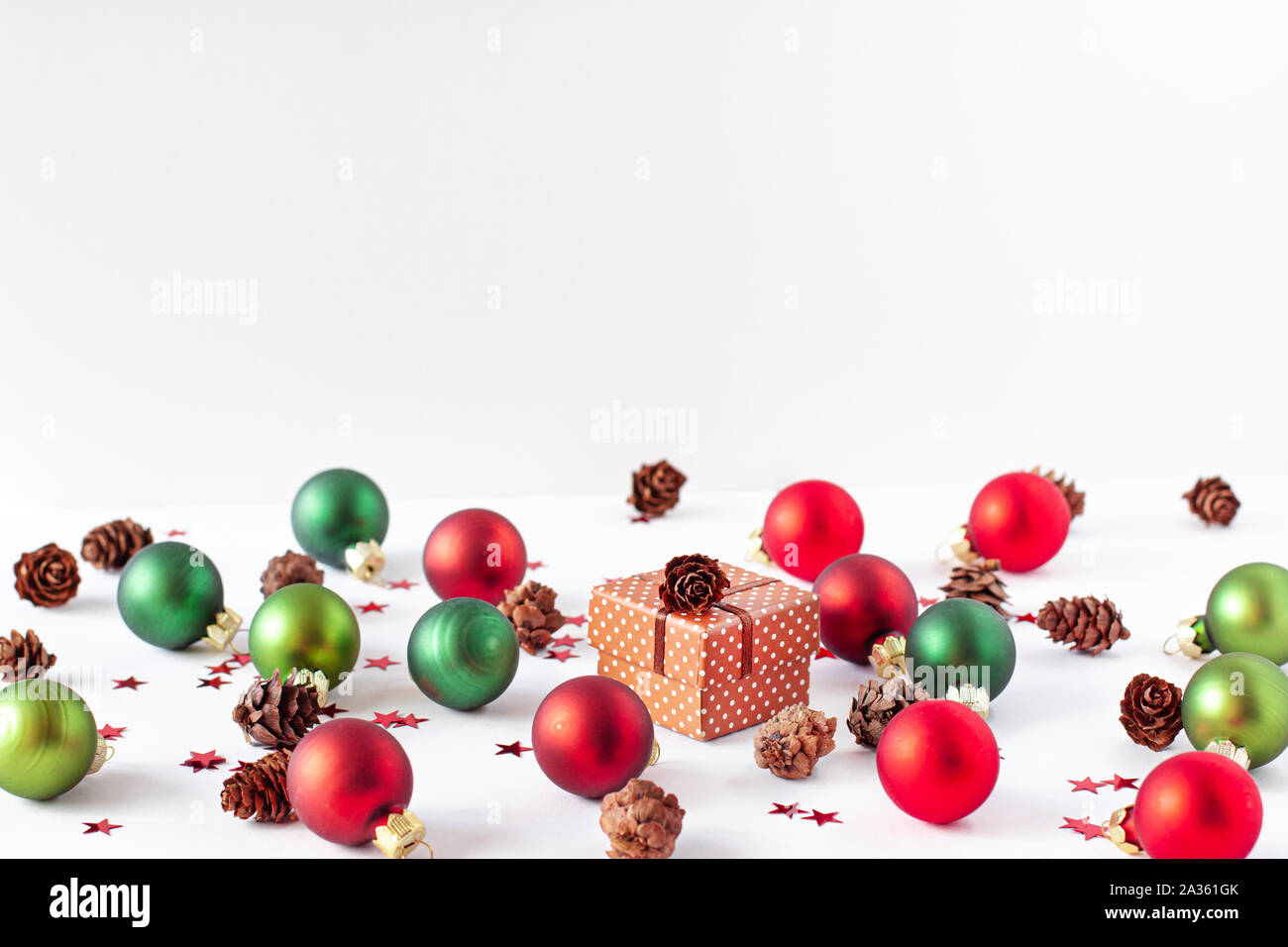 Decorative snow and christmas balls of red and green colors, pine cone, small red stars around and brown present box. Xmas concept with copy space Stock Photo