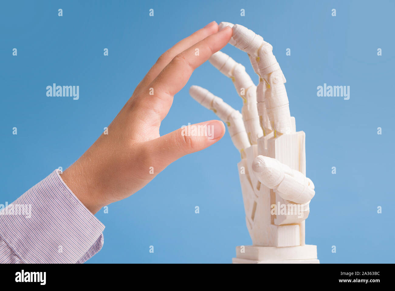 Human and robot hands touching each other, blue background Stock Photo