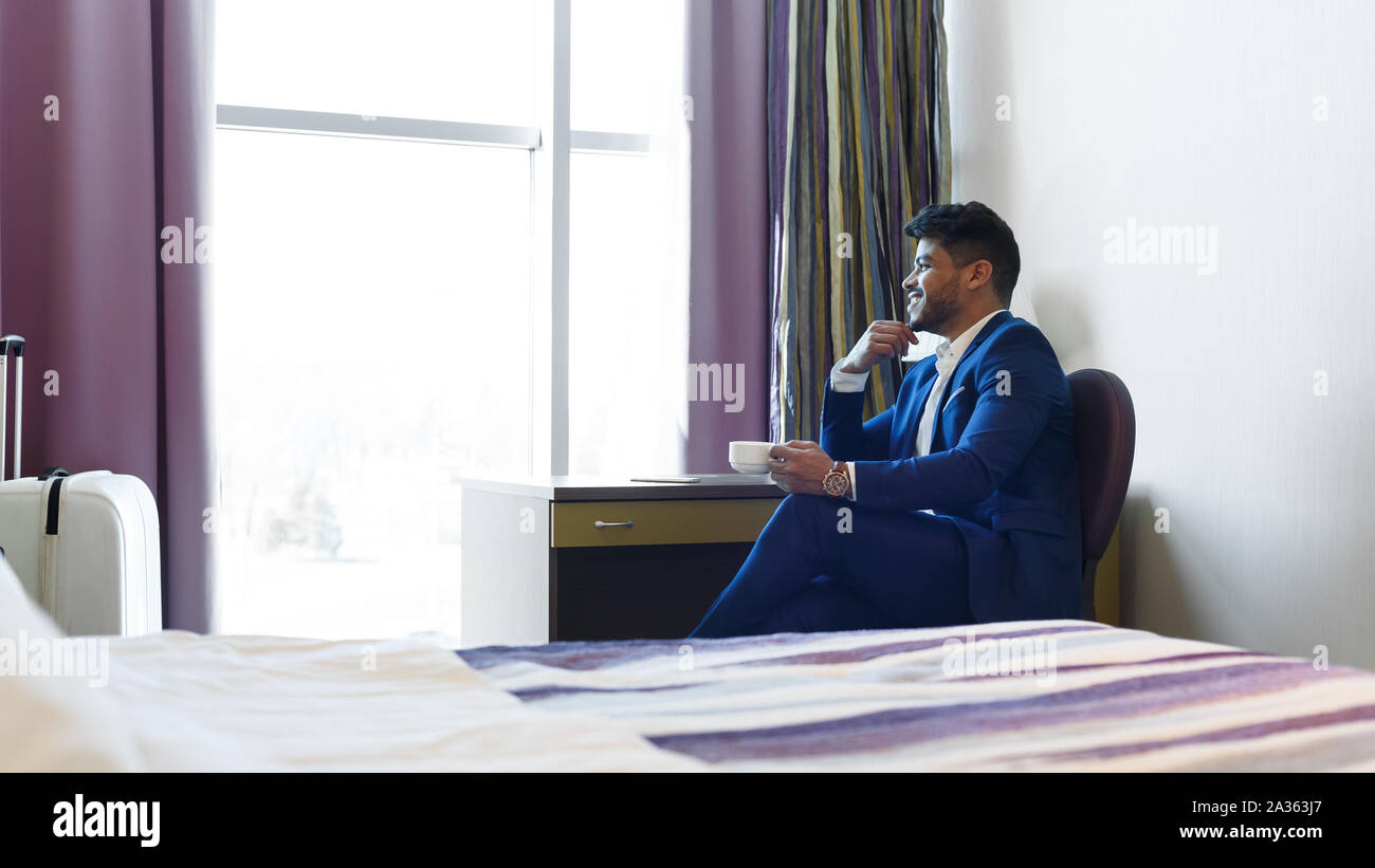 Successful man in suit sitting in hotel room, drinking coffee Stock