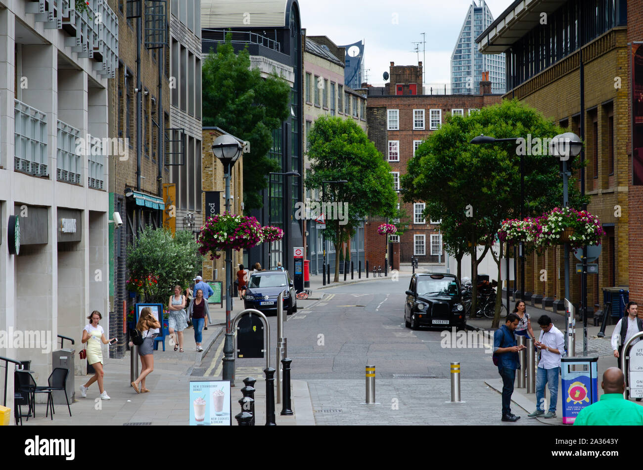 Beautiful London street with flowers, people, green trees and parked black cab. Photo shows 'New Globe walk' street, near Shakespeare's Globe Theatre Stock Photo