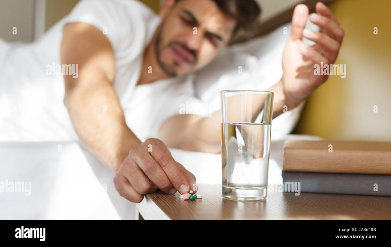Young eastern man taking medicines in bed, feeling sick Stock Photo