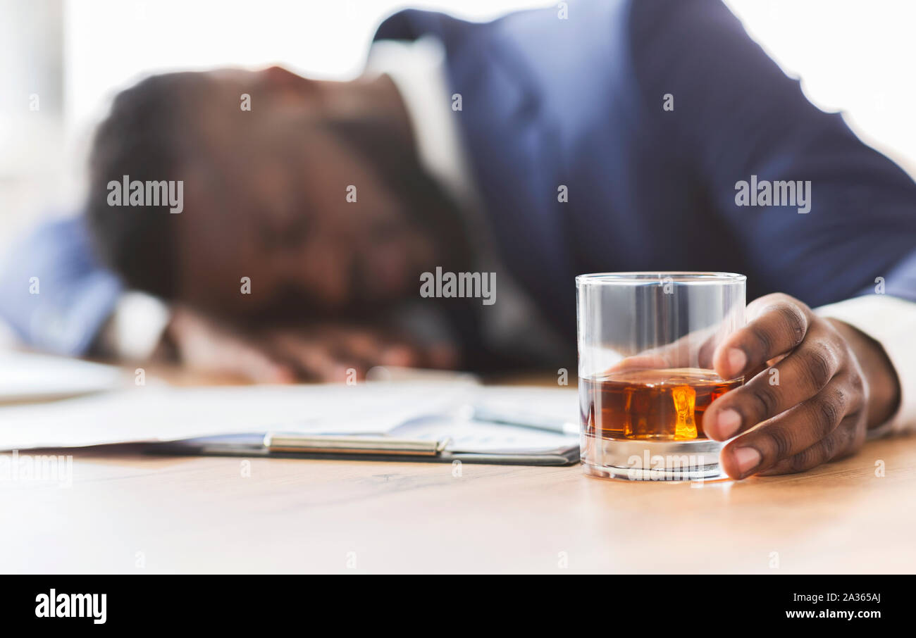 Drunk employee with glass of whiskey sleeping at working place Stock Photo