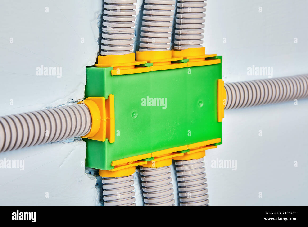 Protecting wires from damage with electrical conduit. Flexible non-metallic electrical conduit connected to a square plastic distribution box. Green j Stock Photo