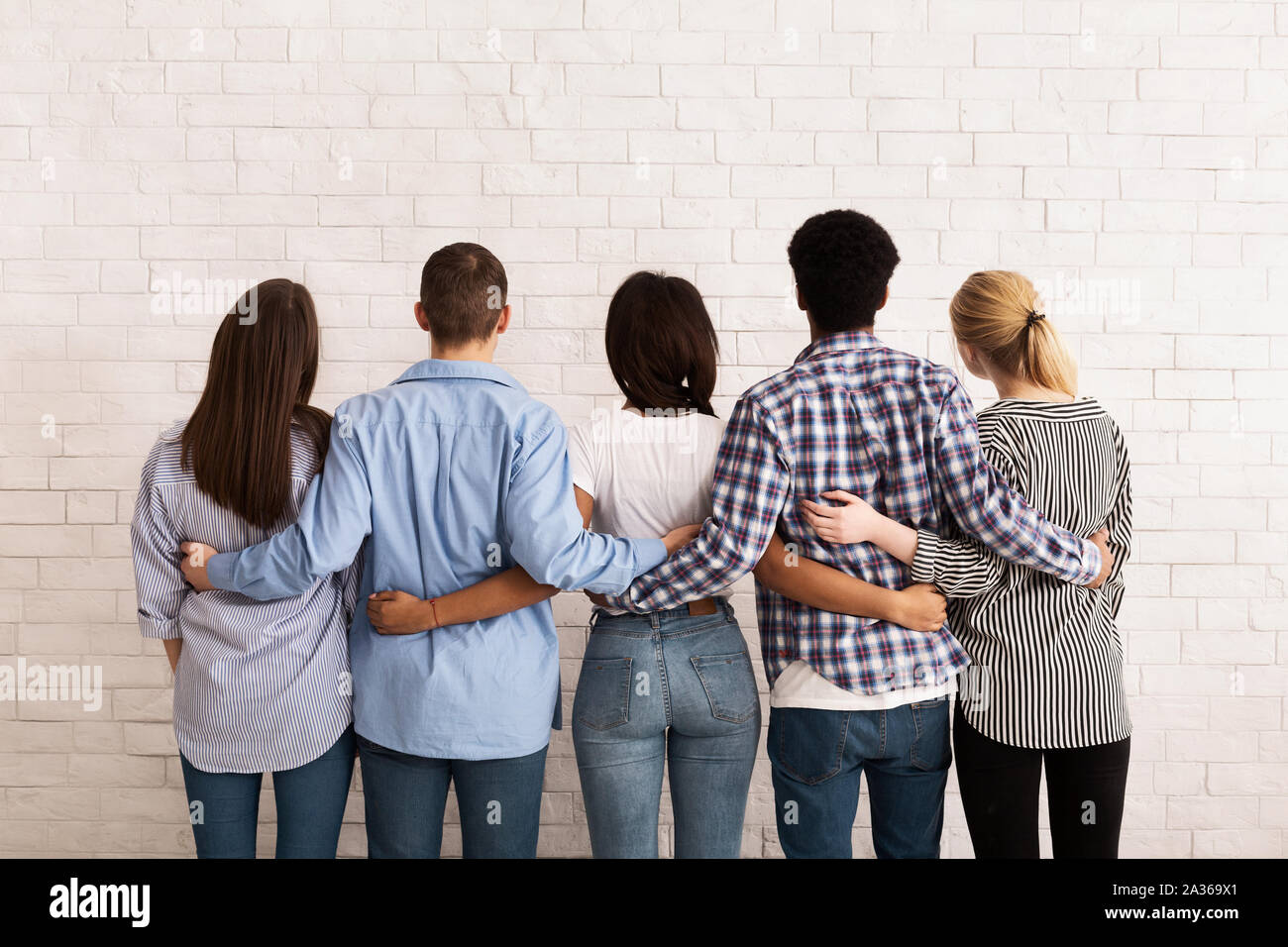 Teen friends embracing and looking at white brick wall Stock Photo