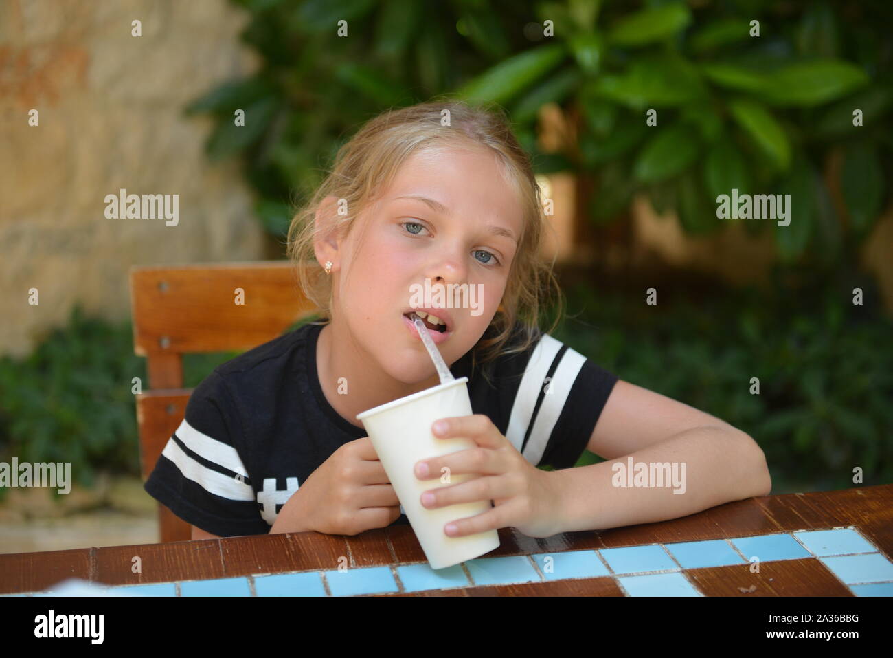 Little girl drinks milk cocktail in a street cafe. Summer holiday Stock